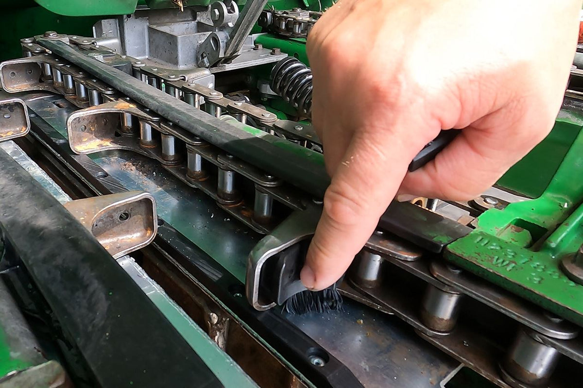 Hand pointing at Kernel Keep rail and brush installed on John Deere corn head.