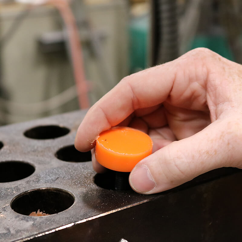 Hand removing orange poly capped bolt from the mold